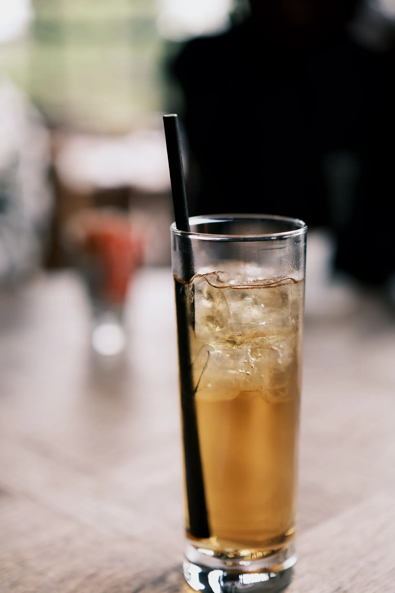 small glass of apple juice with ice cubes floating near the top and a black straw