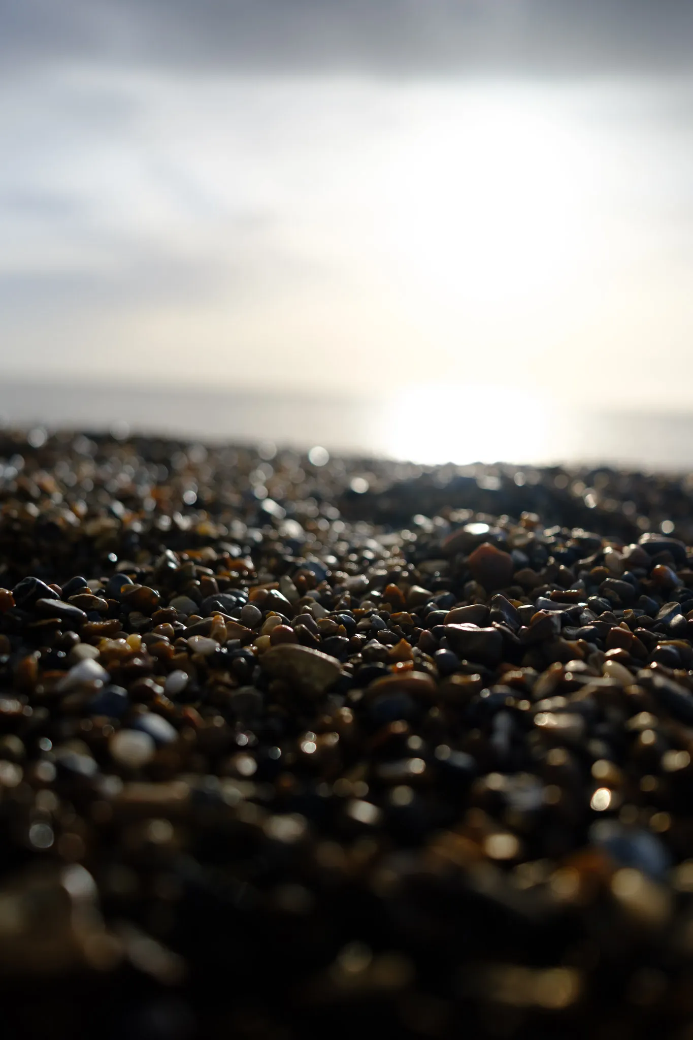 close-up, in-focus shot of a beach filled with pebbles and the bright sky in the background.
